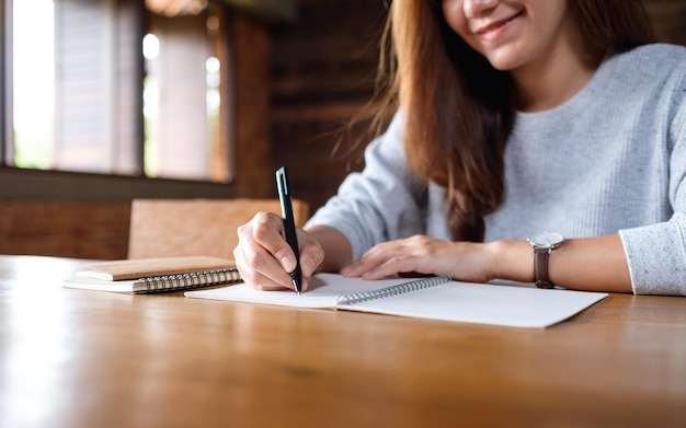 Closeup image of a woman writing on a blank notebook on wooden table