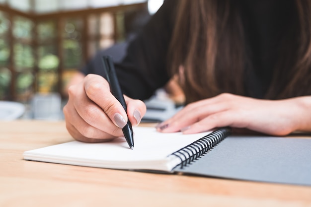 Closeup image of a woman writing down on a white blank notebook on wooden table