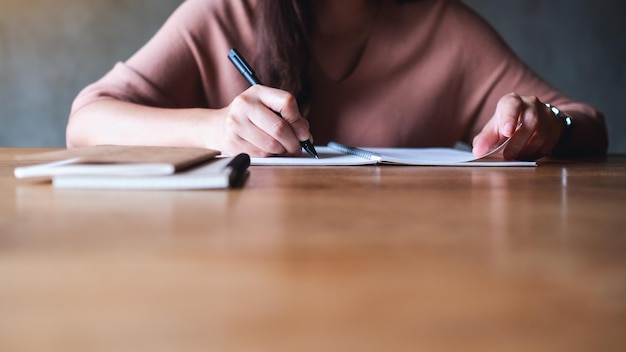 Closeup image of a woman writing on notebook on wooden table