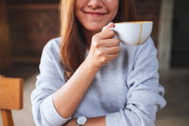 Closeup image of a young asian woman holding and drinking hot coffee