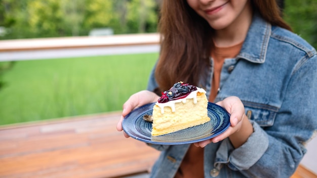 Closeup image of a young asian woman holding and showing a plate of blueberry cheesecake