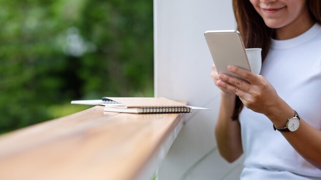 Closeup image of a young asian woman holding and using mobile phone in the outdoors