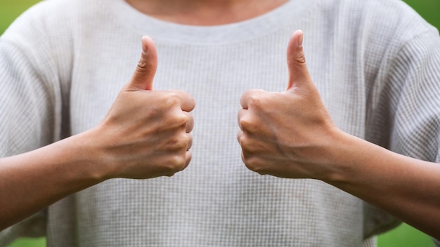 Closeup image of a young woman making and showing thumbs up hand sign