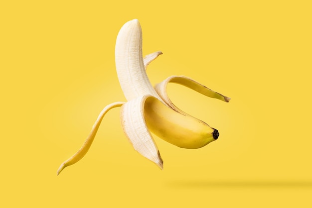 Closeup of isolated fresh banana half peeled and suspended in the air on yellow background