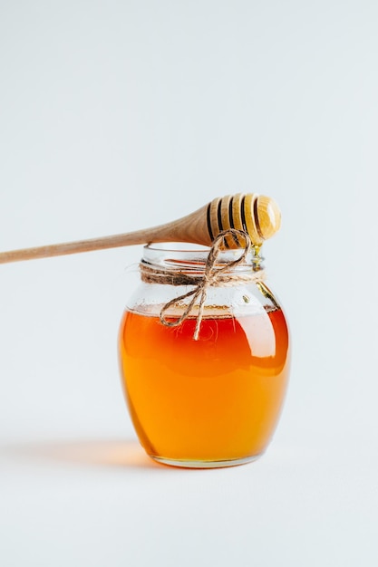 Closeup on a jar of honey and a wooden spindle for honey on a white background