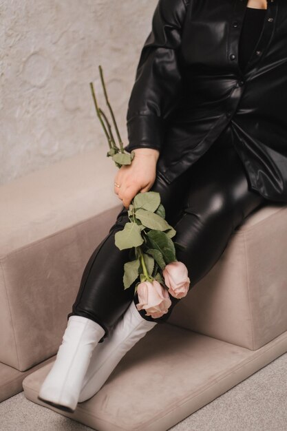 Photo closeup of legs and a bouquet of flowers of a stylish woman in black leather clothes sitting on an ottoman