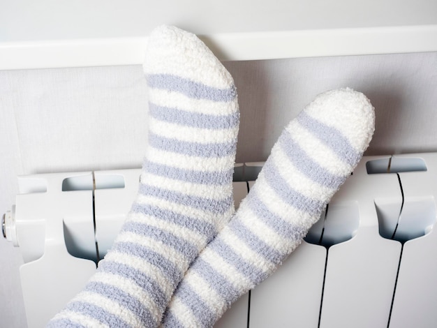 Closeup of legs dressed in warm socks on a white central heating battery The concept of the winter season the heating crisis High gas prices