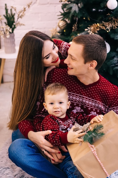 Closeup of little boy holding gift and parents embrace him. family on Christmas tree background.