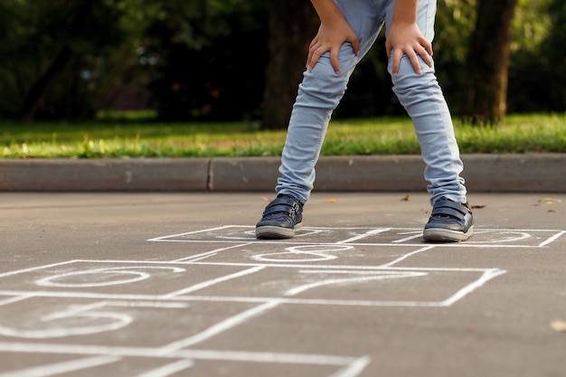 Closeup of little boy's legs and hopscotch drawn on asphalt. Child playing hopscotch game on playground outdoors.