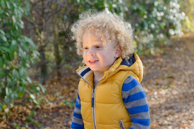 Closeup of little cute boy with blonde curly hair, standing 