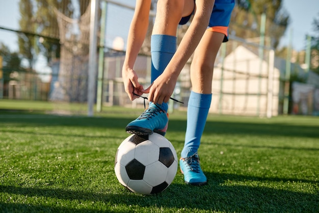 Closeup little football player tying shoelaces putting leg on ball