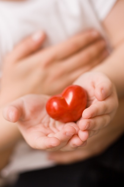 Closeup of a little kid in the arms of a mother with a beautiful red heart in her hands