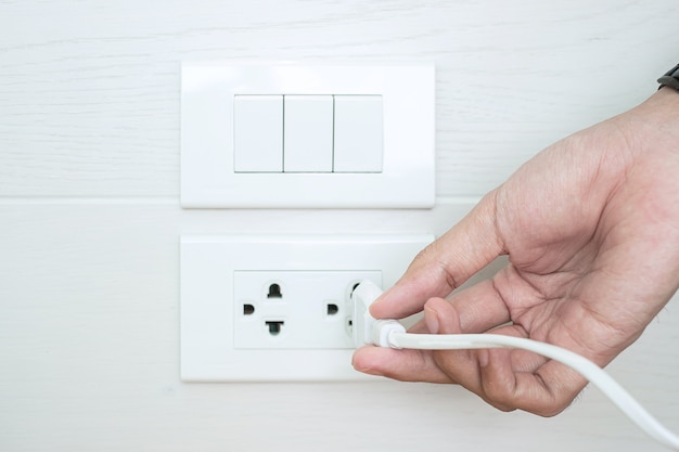 Closeup Male finger unplugging or plugging of electricity device on white wall at home.