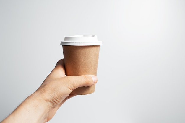 Closeup of male hand holding paper cup of coffee takeaway on white background