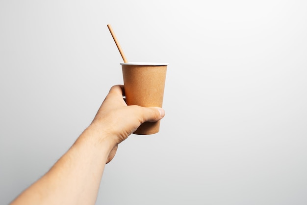 Closeup of male hand holding paper cup of coffee with bamboo straw on white