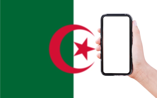 Closeup of male hand holding smartphone with blank on screen on background of blurred flag of Algeria