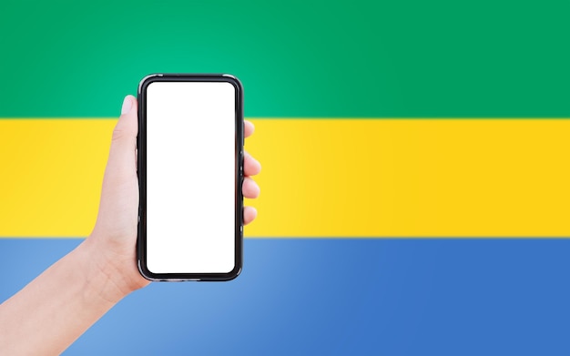 Closeup of male hand holding smartphone with blank on screen on background of blurred flag of Gabon