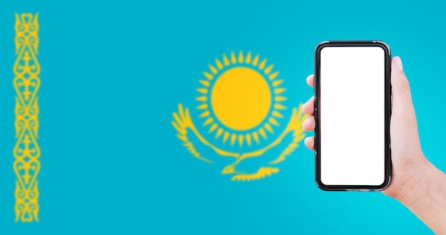 Closeup of male hand holding smartphone with blank on screen on background of blurred flag of Kazakhstan