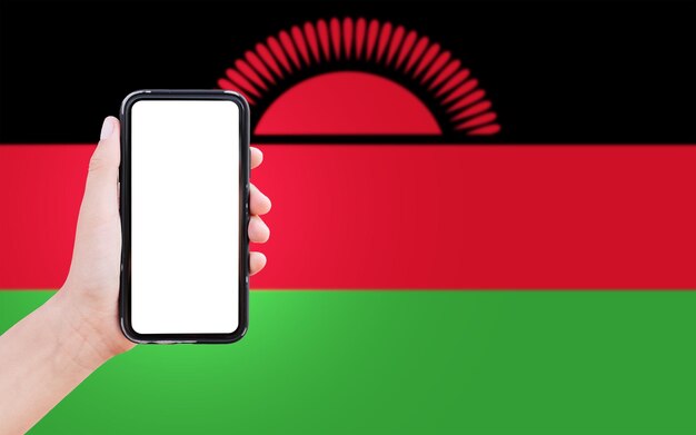 Closeup of male hand holding smartphone with blank on screen on background of blurred flag of Malawi