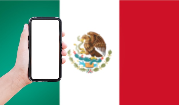 Closeup of male hand holding smartphone with blank on screen on background of blurred flag of Mexico