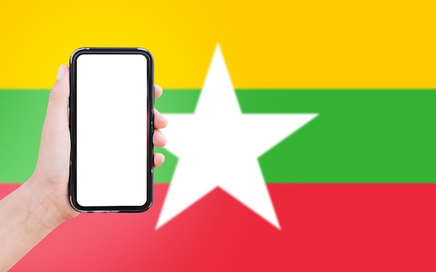 Closeup of male hand holding smartphone with blank on screen on background of blurred flag of Myanmar