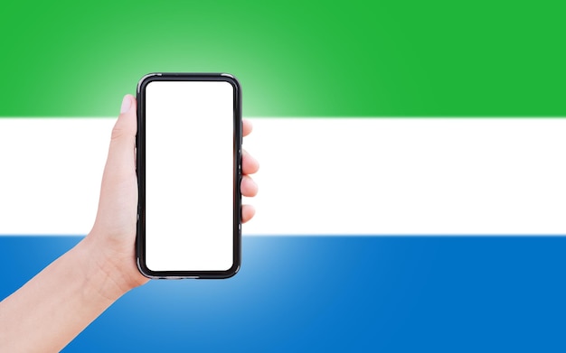 Closeup of male hand holding smartphone with blank on screen on background of blurred flag of Sierra Leone