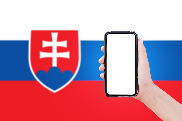 Closeup of male hand holding smartphone with blank on screen on background of blurred flag of Slovakia