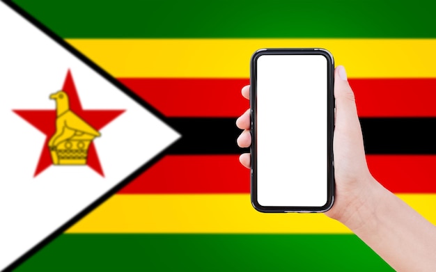 Closeup of male hand holding smartphone with blank on screen on background of blurred flag of Zimbabwe