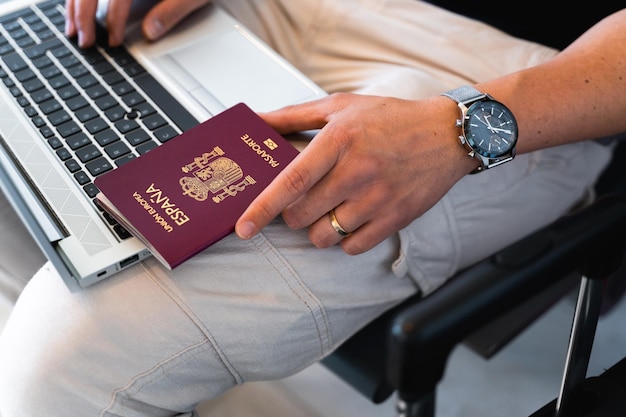 Closeup male hand holding Spanish European passport while using computer laptop Travel concept