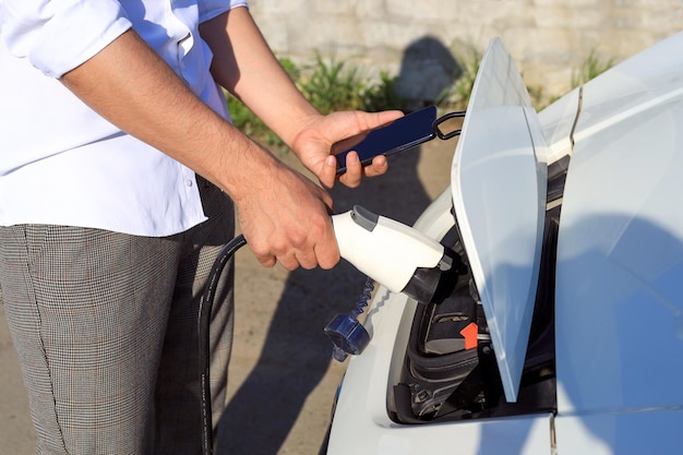 Closeup male hands with a smartphone connect an electric car to a charger