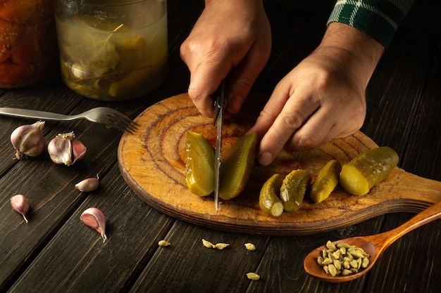 Closeup of a man hands using a knife to cut a pickled cucumber on the kitchen table for preparing a Ukrainian national dish Peasant food