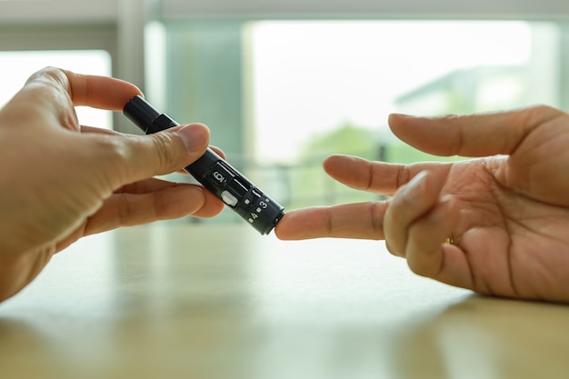 Closeup of man hands using lancet on finger to check blood sugar level by Glucose meter