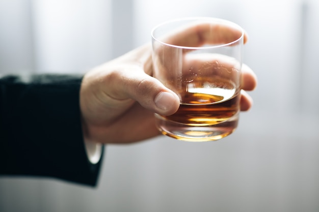 Closeup of man holding glass of whiskey in black suit