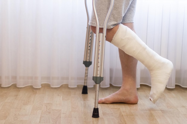 Closeup of man leg in plaster cast using crutches while walking