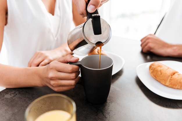 Closeup of man pouring coffee into the cup of his girlfriend on the kitchen