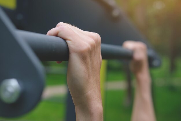 Photo closeup of man's hands on the horizontal pullup bar during outdoor workout in sunlight