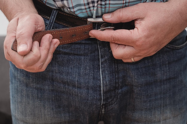 Closeup of a man's hands putting on a pair of jeans and closing the belt