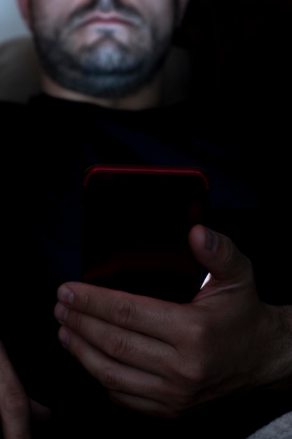 Closeup of a man sitting on the sofa at night making use of the smartphone