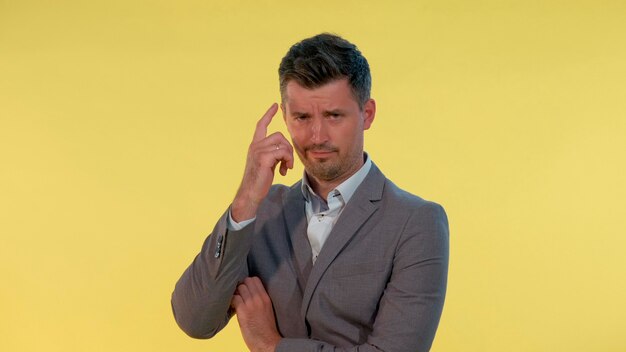 Closeup of man in suit putting his finger to the temple on yellow background he is dissatisfied with...