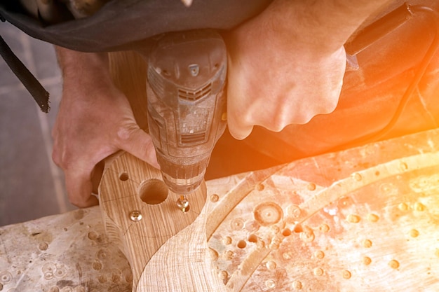 Closeup of a man with work clothes a carpenter drilling a wooden board with screwdriver on wooden table