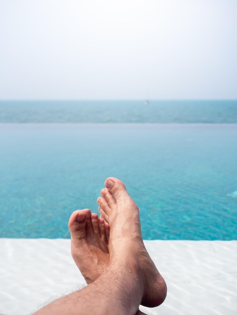 Closeup of the mans foot in the blue water on the tropical pool and sea view Holiday vacation summer background vertical style