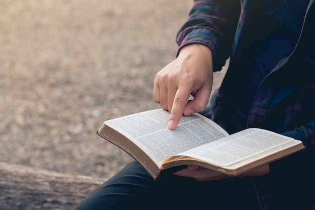 Closeup of mans hands while reading the Bible outsideSunday readings Bible education