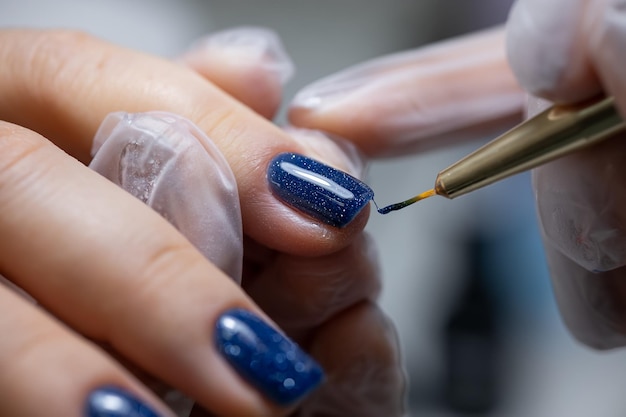 A closeup of the master applies a gel polish with a brush to the surface of the nail under the lamp glowing on them