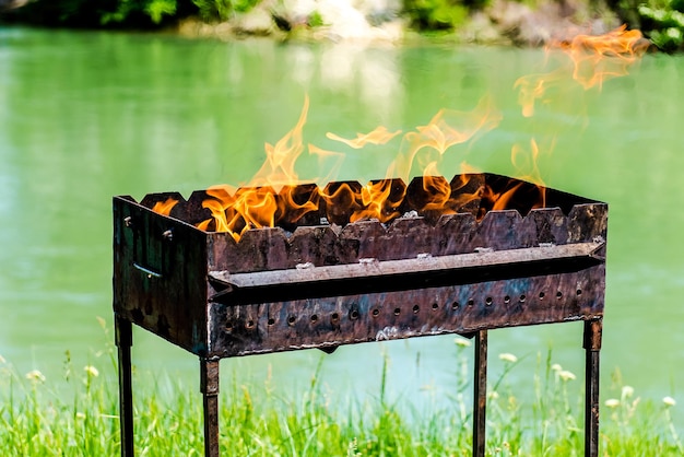 Closeup of a metal brazier with fire on a sunny summer river background Camping concept