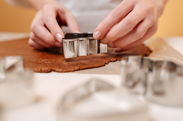 Closeup of a metal christmas tree shape carves a gingerbread dough on the table sweet for christmas ...