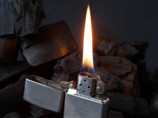 Closeup of metal gas lighter with burning fire on dark coal background with reflections