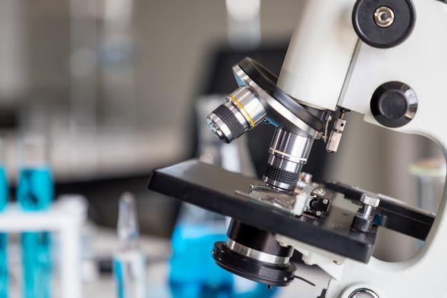 Closeup of microscope examining slide of sample with test tubes in background Concept for science and technology research in laboratory