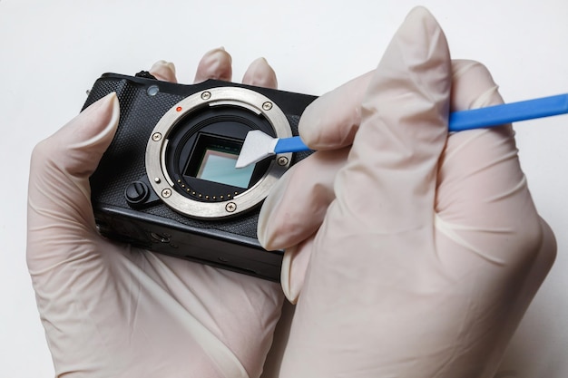 Photo closeup of mirrorless digital apsc dirty camera matrix sensor cleaning and maintenance with swab photographer cleaning photocamera on white background