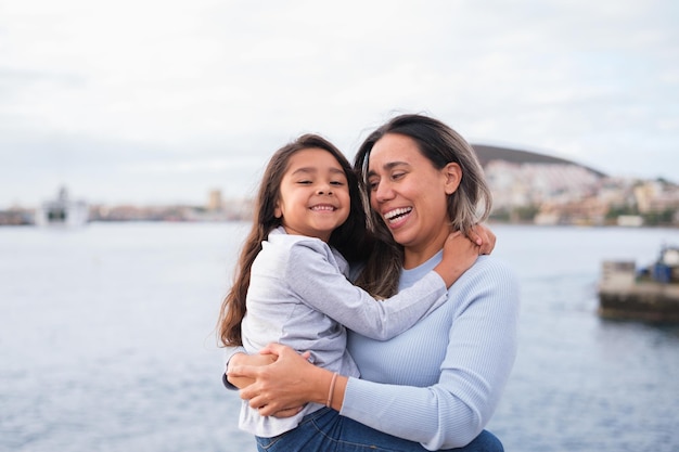 Closeup of mother with her young daughter in her arms and cuddling by the sea on a gray day Concept Maternity lifestyle outdoors