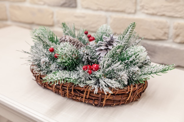 Closeup New Year wicker basket with snow covered spruce evergreen branches, cones red berries.  christmas decor, table decoration, hand made